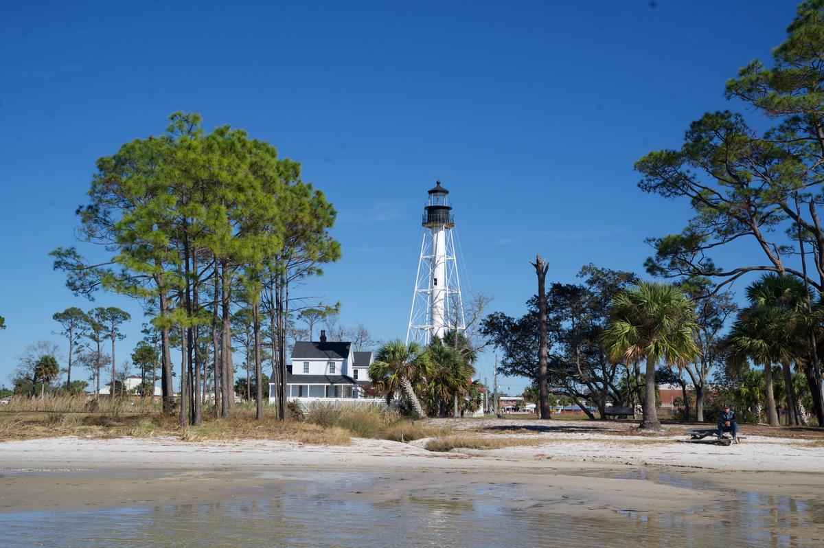 Scenic view of Cape San Blas Lighthouse surrounded by trees and a sandy beach under a clear blue sky