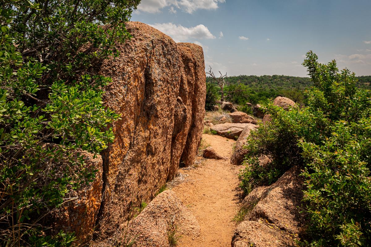 Granite boulders and rugged dirt trail surrounded by greenery at Enchanted Rock in Fredericksburg