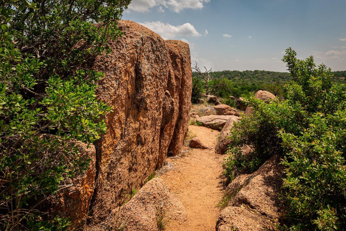 Granite boulders and rugged dirt trail surrounded by greenery at Enchanted Rock in Fredericksburg
