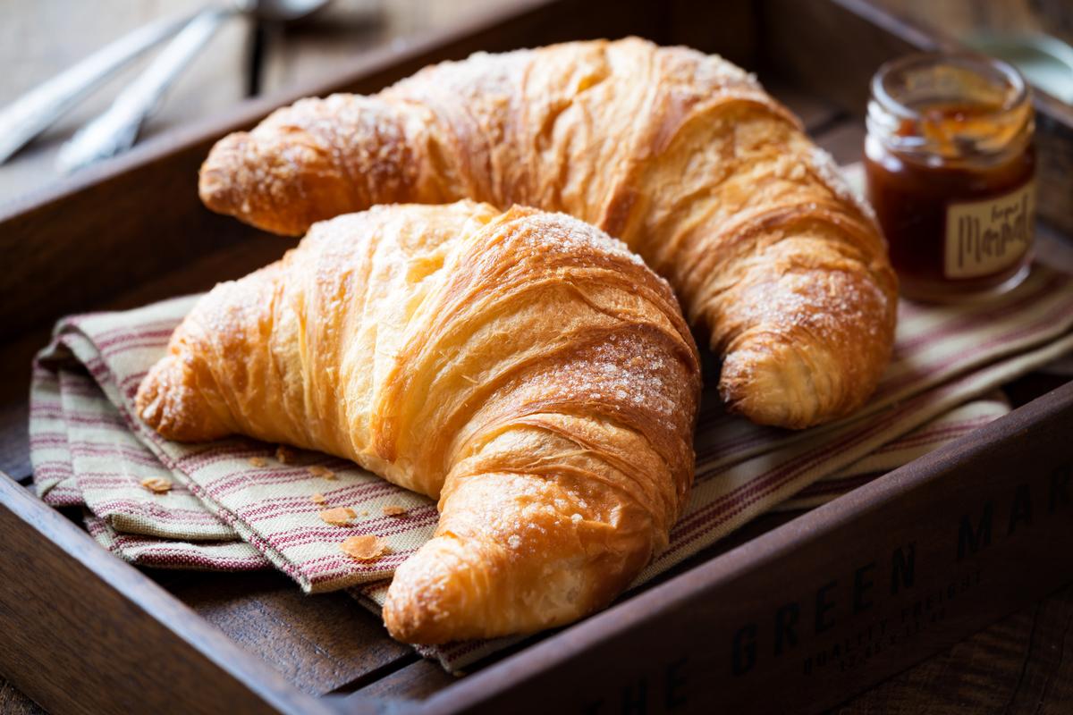 Freshly baked croissants on a tray with a small jar of jam for breakfast